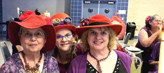 Three smiling Red Hatters in red hats and purple tops at the murder mystery wedding.